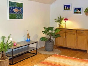 A living room with a wooden floor, a dining table with a plant, a cabinet, and framed artwork on the wall.