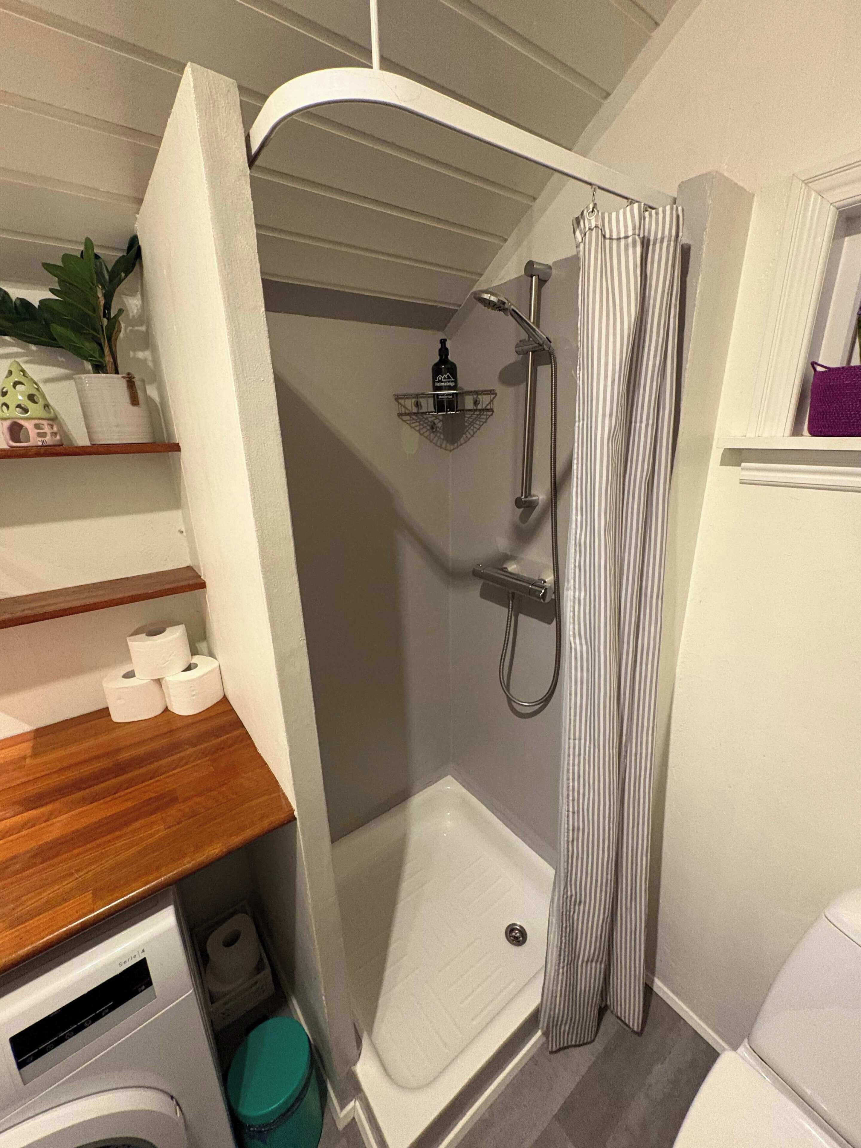A compact bathroom with a shower, toilet, and a small shelf with toiletries.