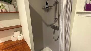 A compact bathroom with a shower, toilet, and a small shelf with toiletries.