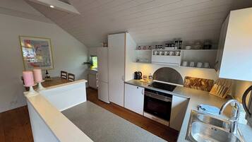 Ett kompakt kök med vita skåp, en inbyggd ugn, en diskho och en matplats med ett bord och stolar.