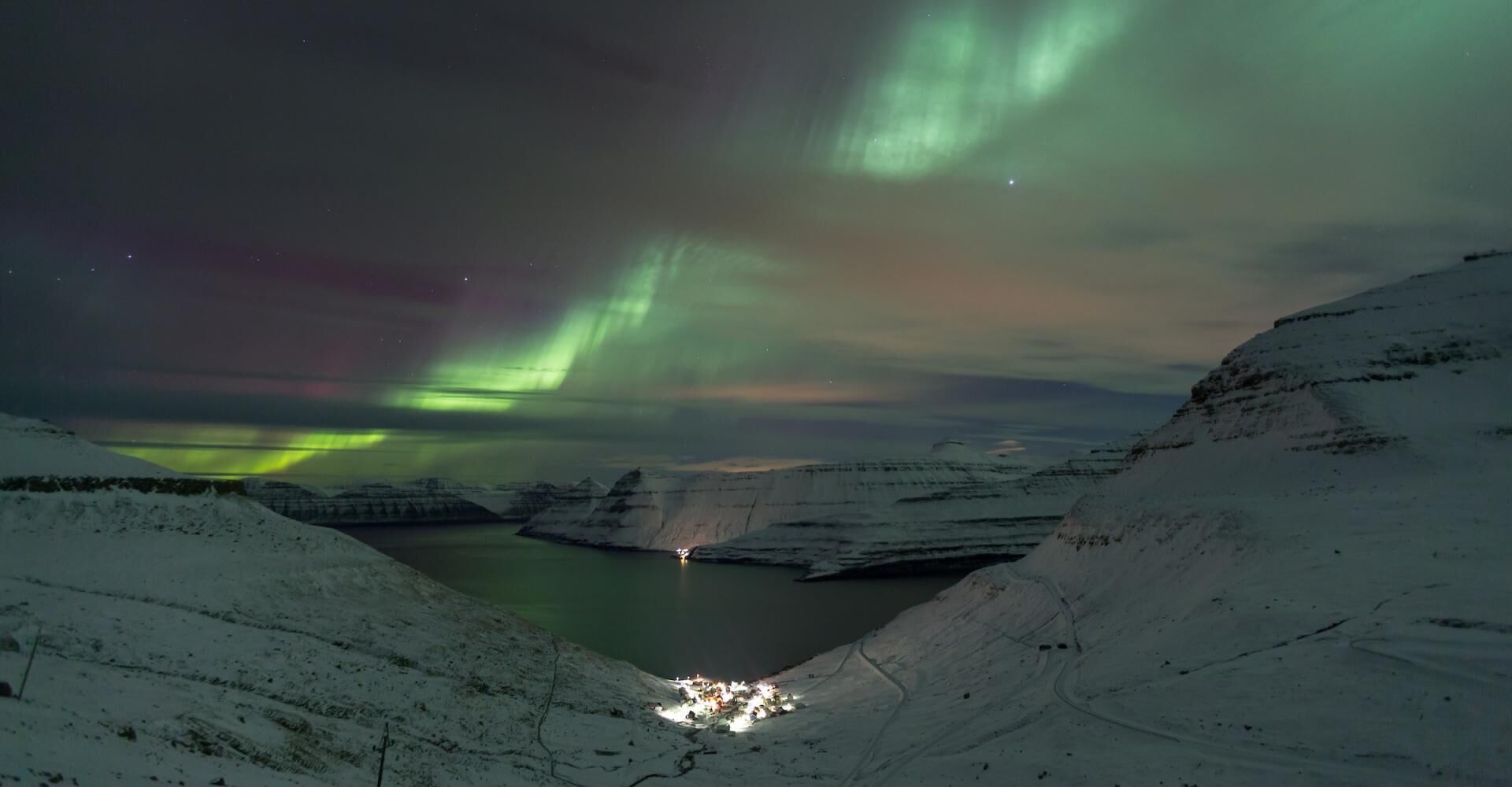 Un paisaje nevado con un río y un pequeño asentamiento a su base.