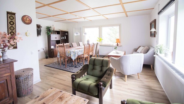 Um quarto bem iluminado com área de jantar, um espaço de estar com sofá e cozinha ao fundo.