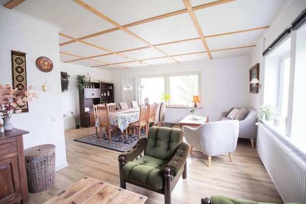 A well-lit room with a dining area, a seating area with a sofa, and a kitchen in the background. - Grand Fjordview Villa - Sleeps 15 & 3 Baths (Vestmanna)