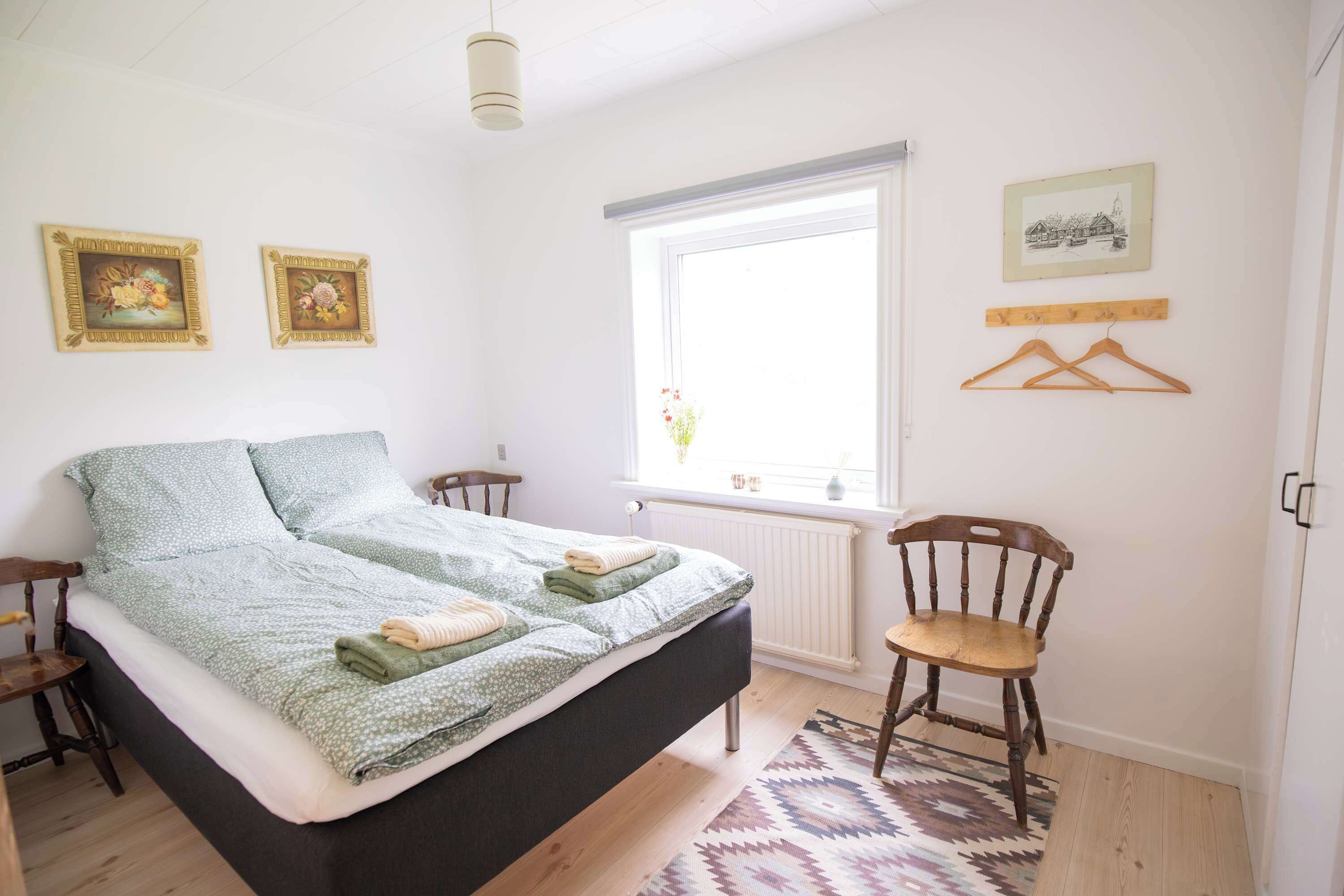 Een slaapkamer met een bed, een stoel, een raam en spullen aan de muur.