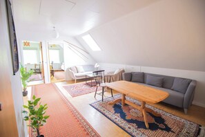 A spacious loft with a high ceiling, a gray sofa, a wooden coffee table, and a patterned rug.