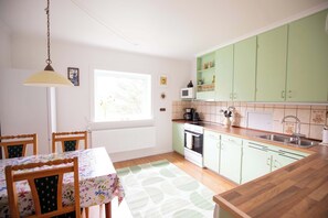 Una cocina con mesa, sillas, lámpara colgante y armarios verdes.
