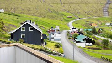Un paysage rural avec une route sinueuse, des maisons et un bâtiment noir imposant.