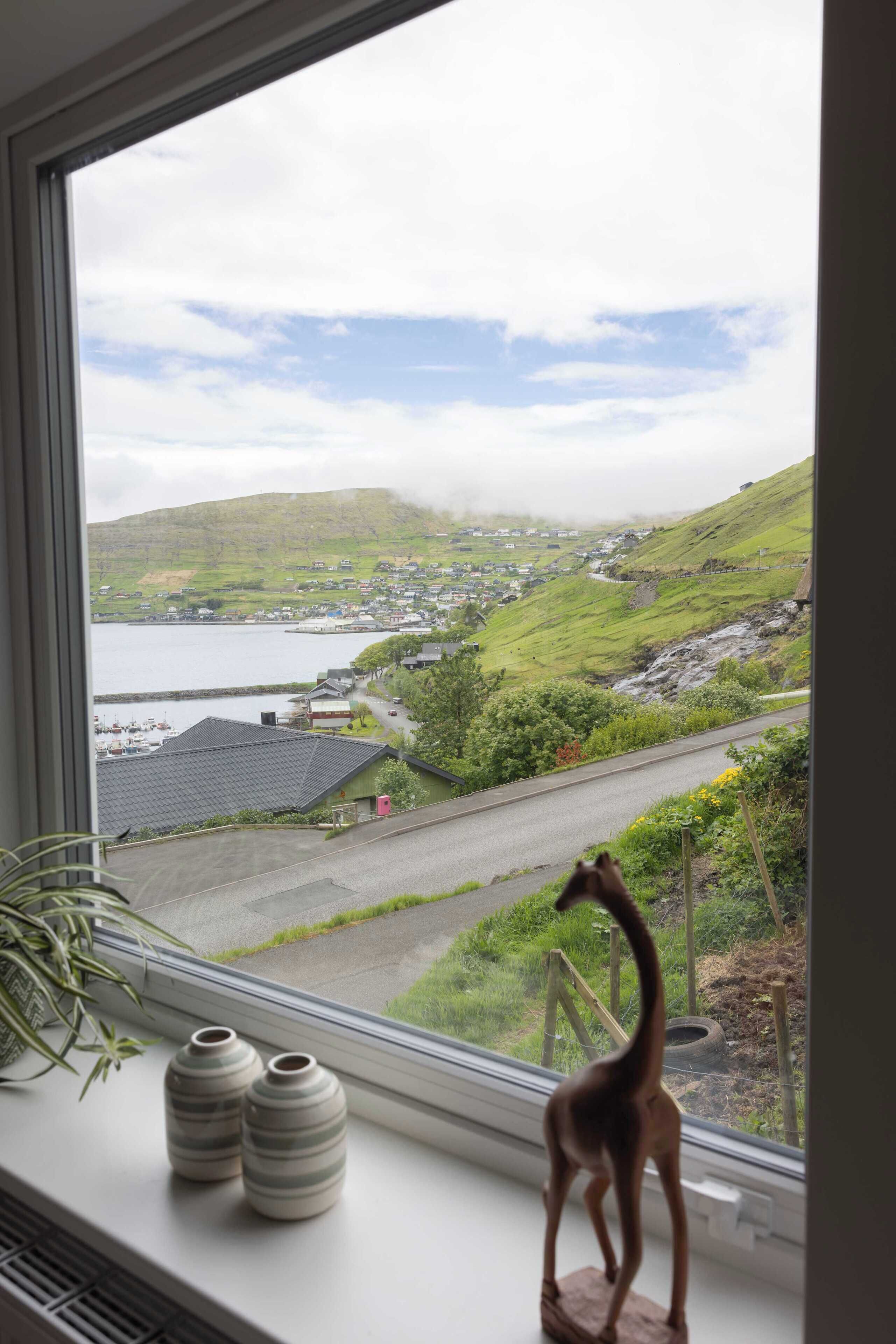 A window with a view of a coastal town, a giraffe figurine, and two ceramic vases on a windowsill.