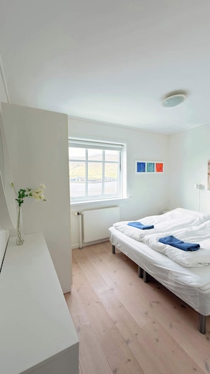 A bedroom with a bed, a window, a radiator, and a vase with flowers.
