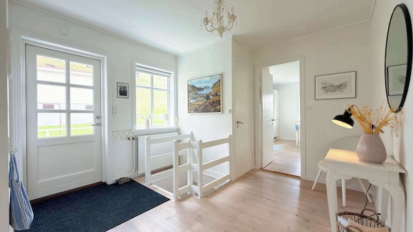 A room with a white door, a black mat, a white bench, a painting, and a vase with dried plants.
