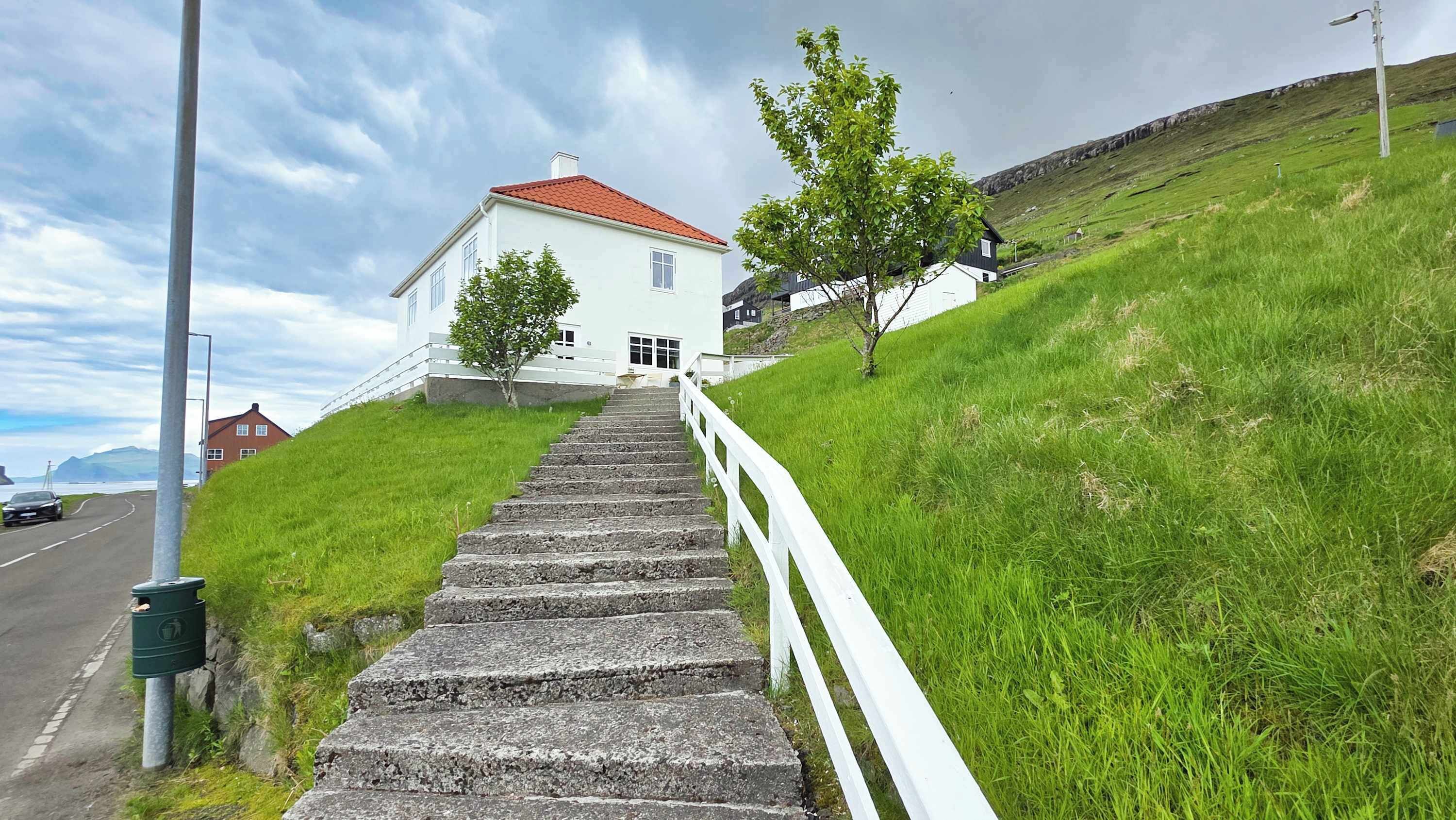 Un escalier mène à un bâtiment blanc surmonté d’un toit rouge, situé sur une colline verdoyante.