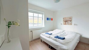 A bedroom with a bed, a window, a radiator, and a vase with flowers. - Oceanfront Home Near Vagar Airport (Sørvágur)