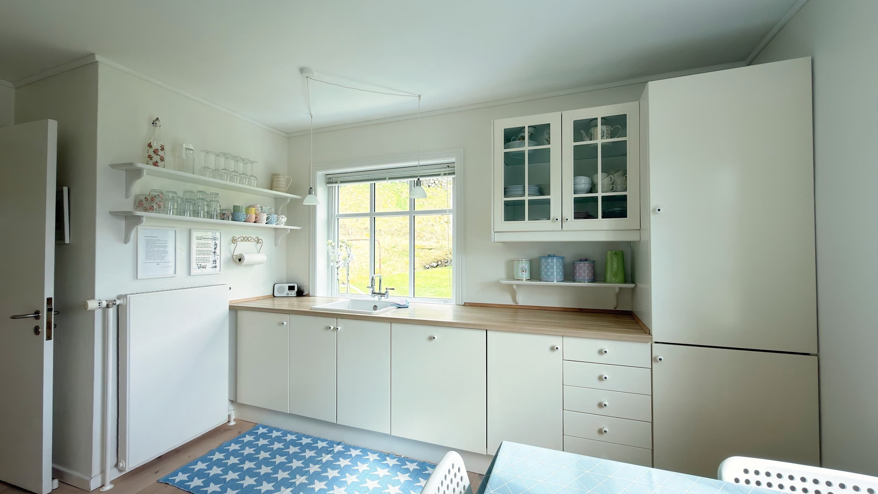 A kitchen with white cabinets, a window, and a blue star-patterned rug.