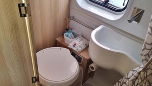 A compact bathroom with a toilet, bidet, and a small shelf with toiletries. - Adventure Autocamper Van to Explore the Faroes (Hoyvík)