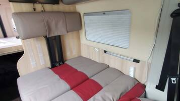 Un intérieur de camping-car compact comprenant un lit, une petite table et une fenêtre.