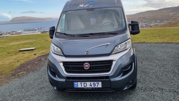 A Fiat van with a camper shell parked on a gravel road with a view of a coastal landscape. - Adventure Autocamper Van to Explore the Faroes (Hoyvík)