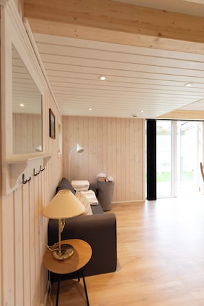 A room with a wooden ceiling, a sofa, a lamp, a mirror, and a window.