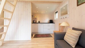 A cozy cabin interior with a wooden staircase, a kitchen area, a sofa, and a lamp.