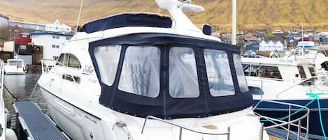 En vit lyxyacht låg förtöjd vid en småbåtshamn, med ett takbeklätt däck och en hytt.