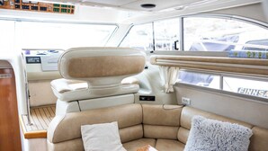 A boat interior with a cushioned seating area, a control panel, and a window with a view of the outside.