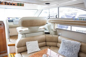 A boat interior with a cushioned seating area, a control panel, and a window with a view of the outside.