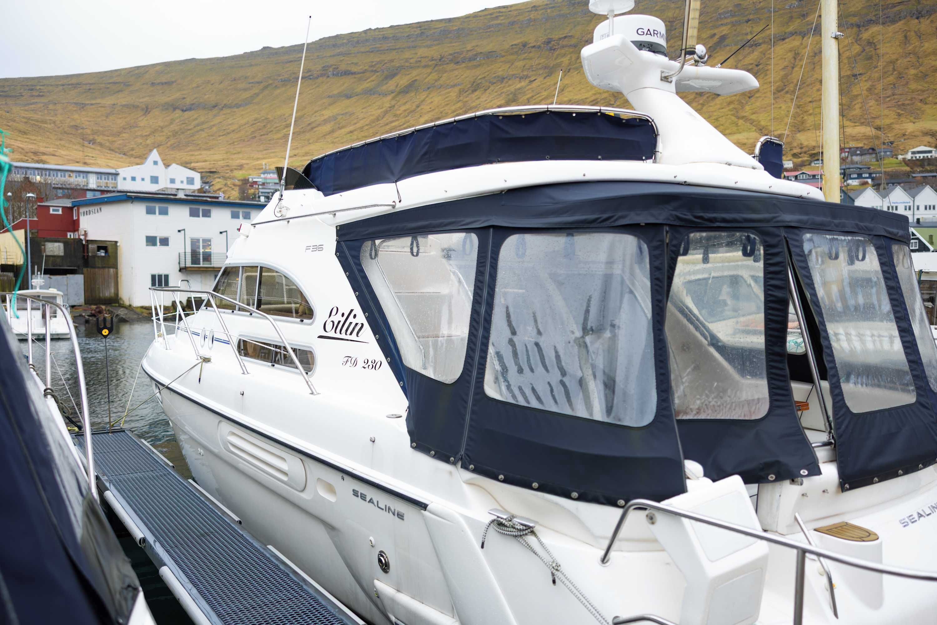 Un yate blanco amarrado en un puerto deportivo, con una cabina cubierta y camarote visible.