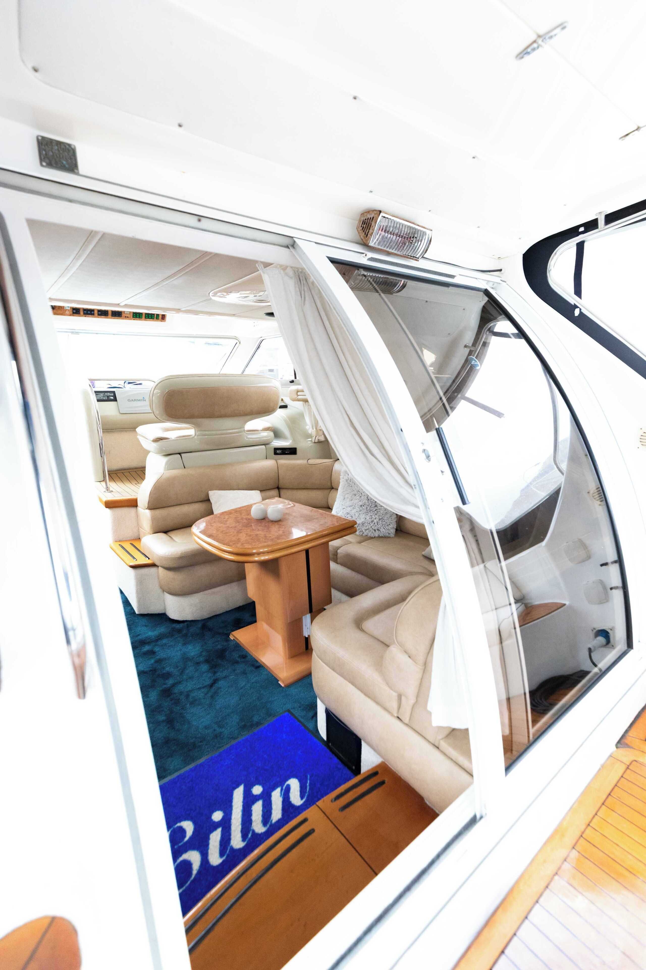 A boat interior with a dining area, cushioned seating, and a blue rug with 'Bilin' text.