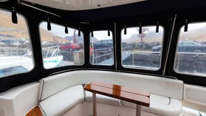 A boat interior with a central seating area, windows, and a view of the outside.