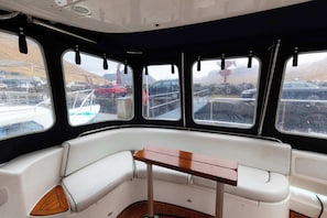 A boat interior with a central seating area, windows, and a view of the outside.