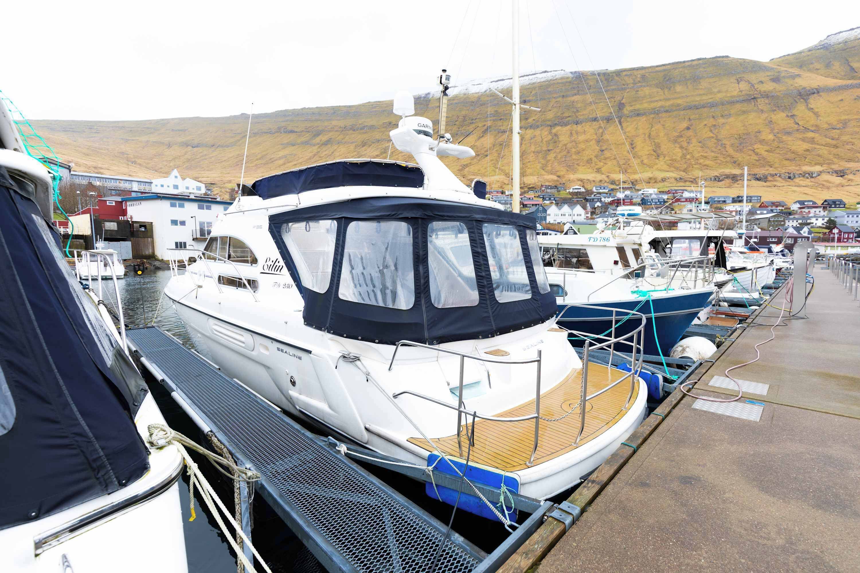 A marina with boats docked, a covered boat in the foreground, and a town in the background.