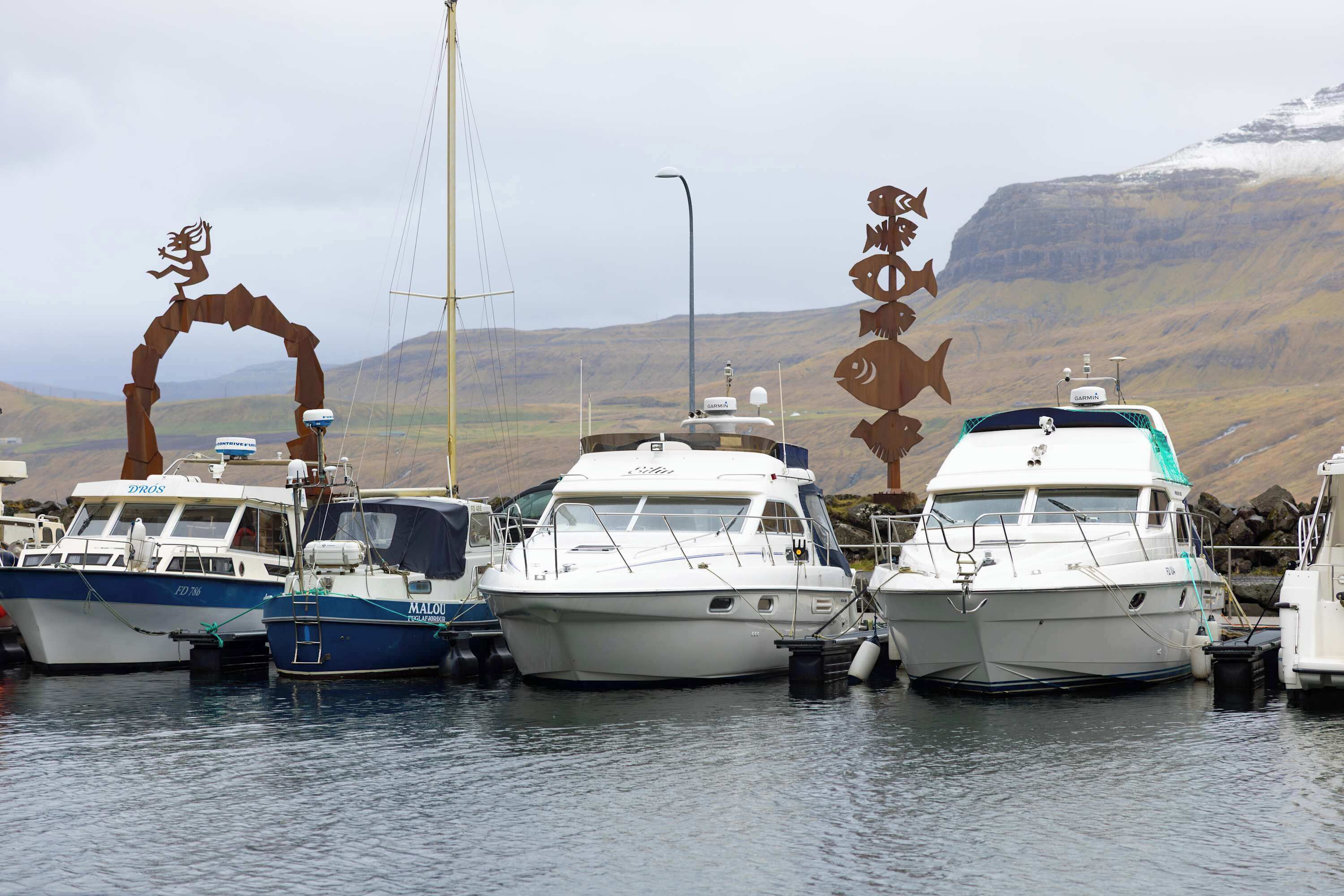 A marina with several boats docked, a mountainous backdrop, and a clear sky.