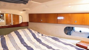 A compact interior with a bed, wooden cabinets, a mirror, and a small window.