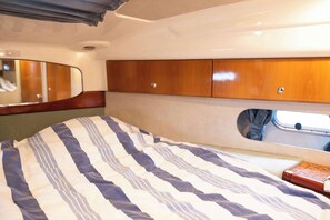 A compact interior with a bed, wooden cabinets, a mirror, and a small window.