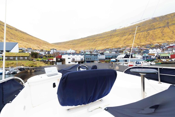 A boat's deck with a covered seating area, a steering wheel, and a Garmin device. In the background, there is a small town with houses and boats docked along the waterfront.