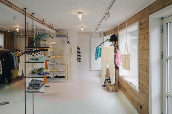 Un magasin de vêtements avec des portants remplis de vêtements, des étagères où sont pliés les articles et une vitrine où sont exposés des vêtements suspendus.