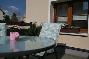 Ein runder Glastisch mit einer rosafarbenen Vase, zwei stilvolle Stühle und ein Fenster mit Blumenkasten.