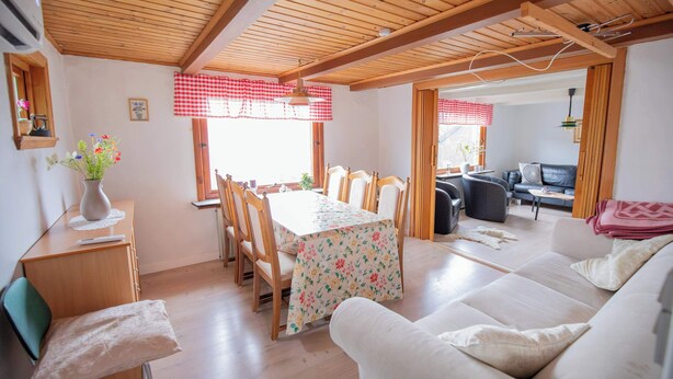A cozy living room with a dining area, wooden ceiling beams, and a sofa.