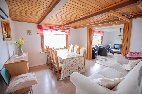 A cozy living room with a dining area, wooden ceiling beams, and a sofa. - Charming Home in Sandavagur Near the Airport (Sandavágur)