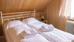 A single bed with white linens and towels, a nightstand with a lamp, and a window with curtains.