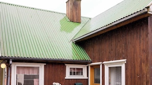 A wooden house with a green roof, a front door, and a small patio area with a table and chairs.