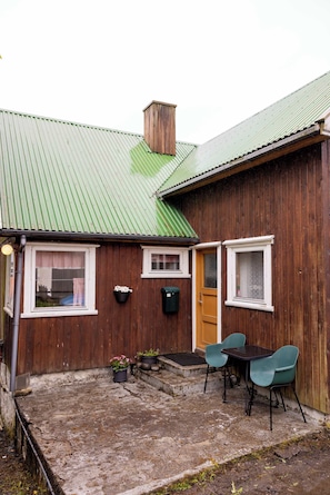 A wooden house with a green roof, a front door, and a small patio area with a table and chairs. - Charming Home in Sandavagur Near the Airport (Sandavágur)
