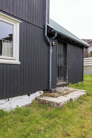 A dark wooden building with a white window and a door, a visible gutter, and a stone ledge. - Traditional Faroese House Near Airport (Sørvágur)