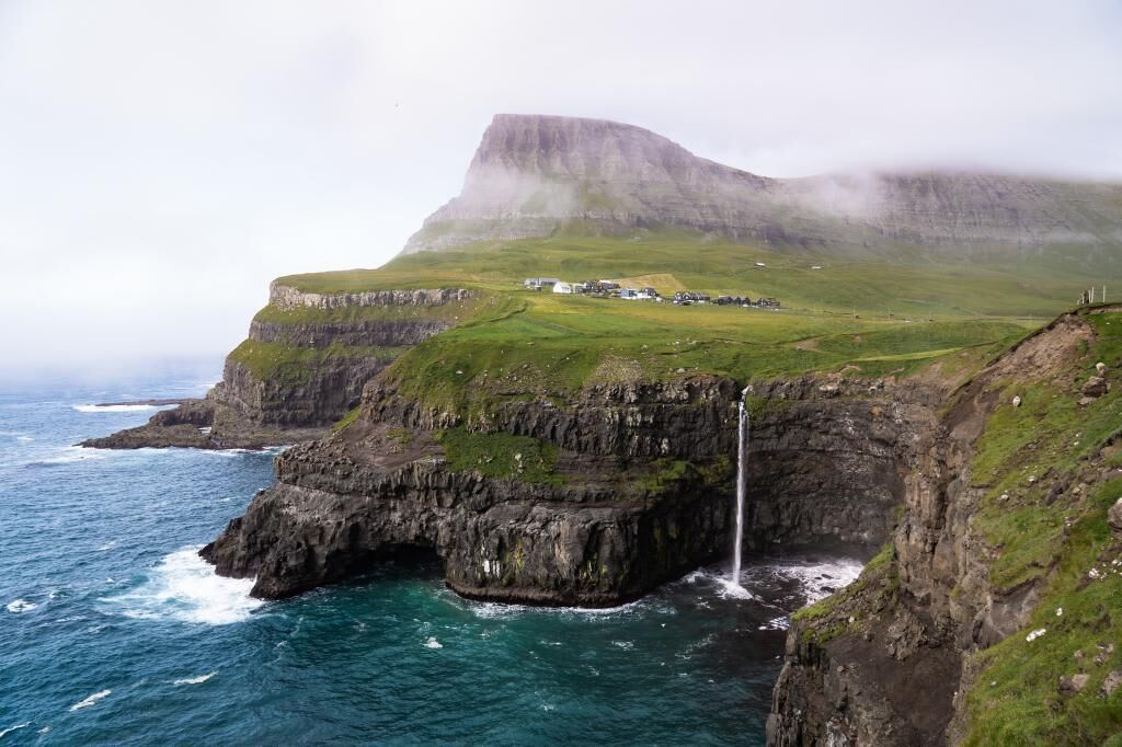 A coastal landscape with a waterfall, cliffs, and a small settlement.