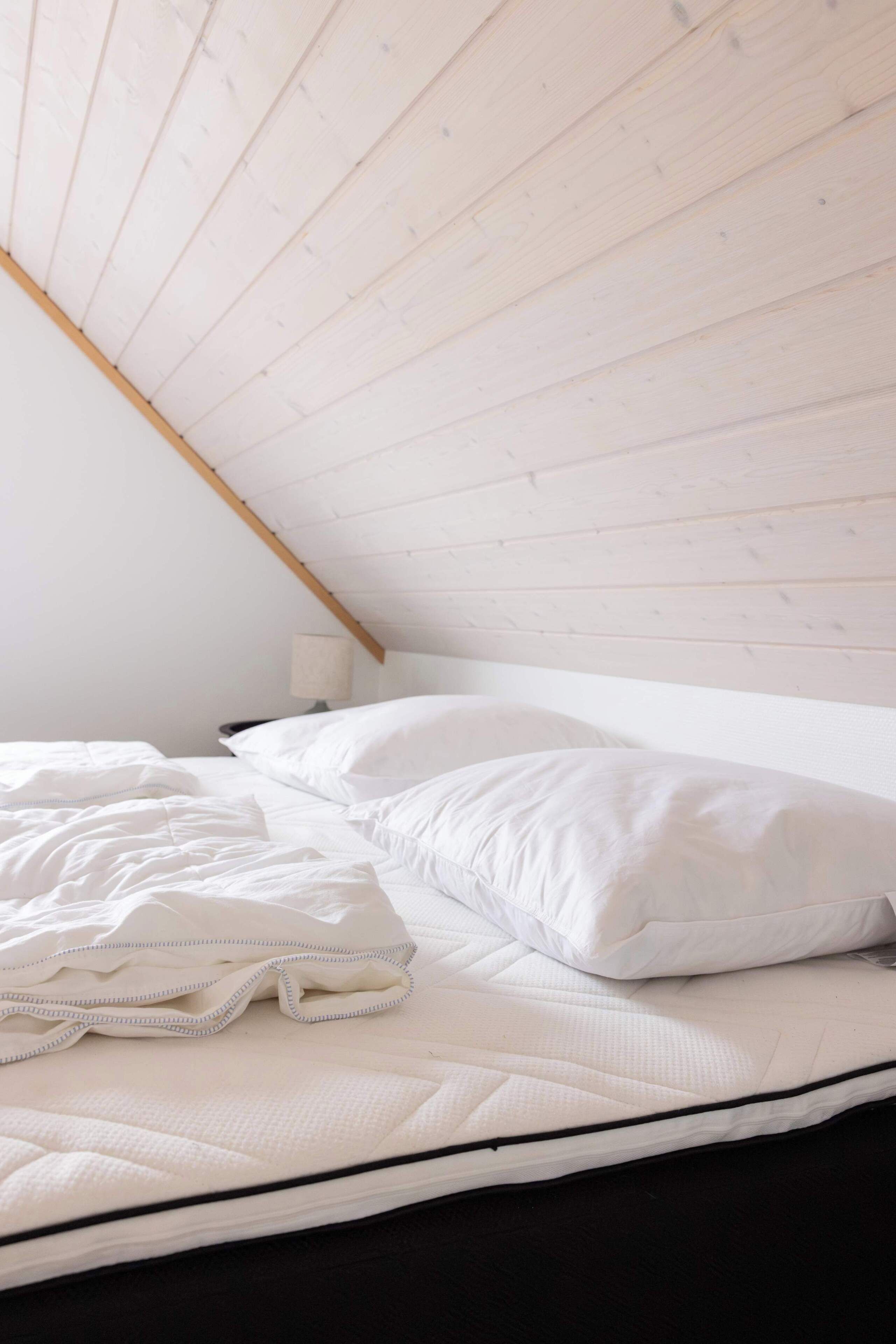 A bedroom with a sloped ceiling, a bed with white bedding, and a nightstand with a lamp.