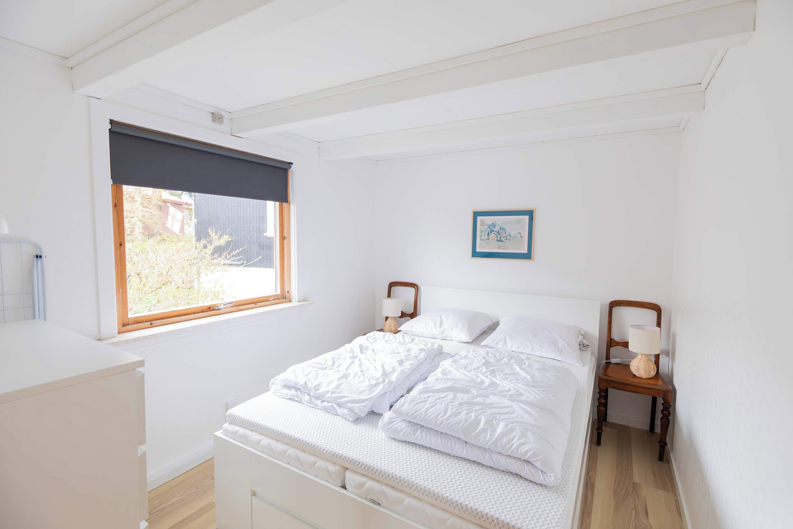 Un dormitorio con una cama, mesitas de noche, una ventana y un cuadro en la pared.