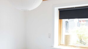 A bedroom with a bed, a bedside table, a window with a view, and a hanging light fixture.