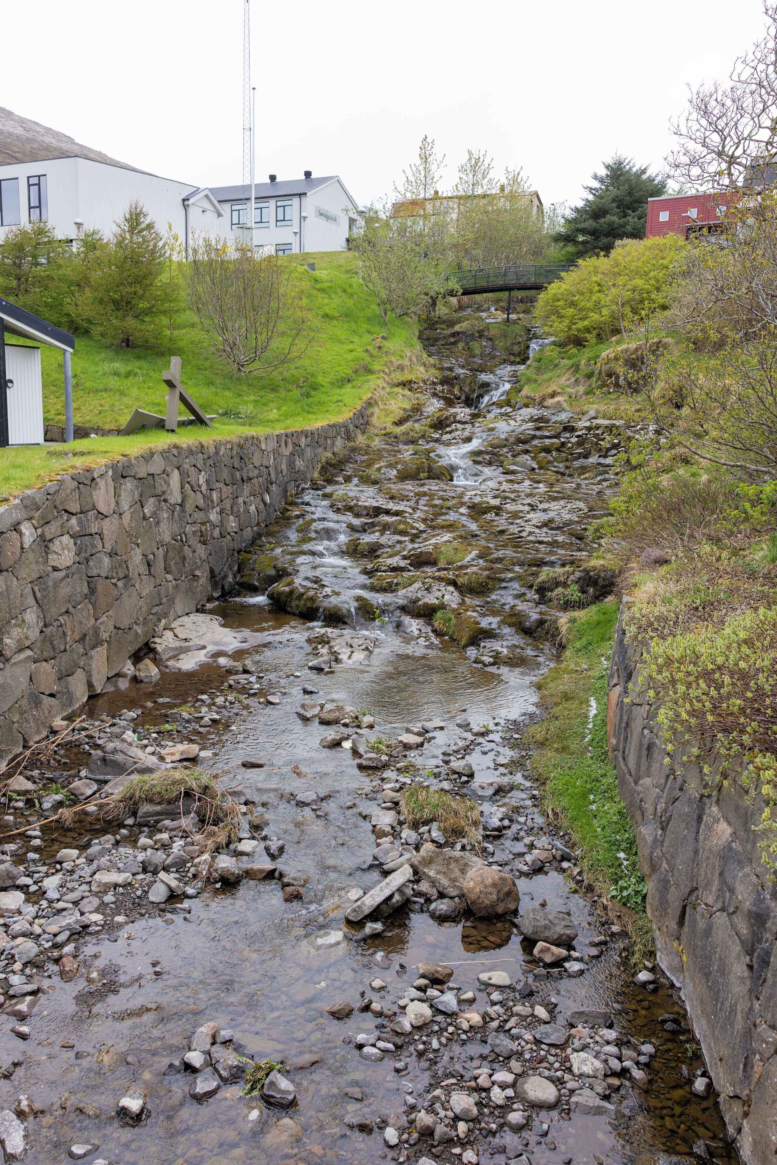 Un arroyo estrecho con un muro de piedra a un lado y un edificio al otro.