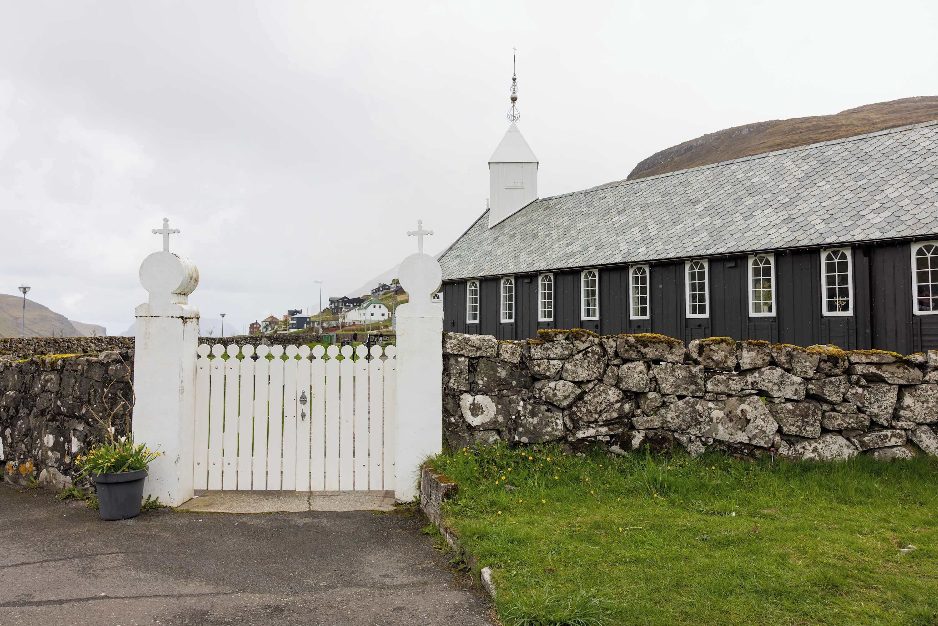 A church with a white fence, stone wall, and a grey roof.