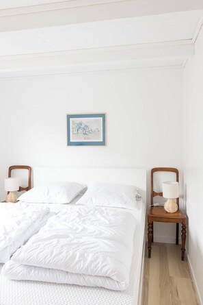 A neatly made bed with white linens, a framed picture on the wall, and two bedside tables with lamps. - Traditional Faroese House Near Airport (Sørvágur)