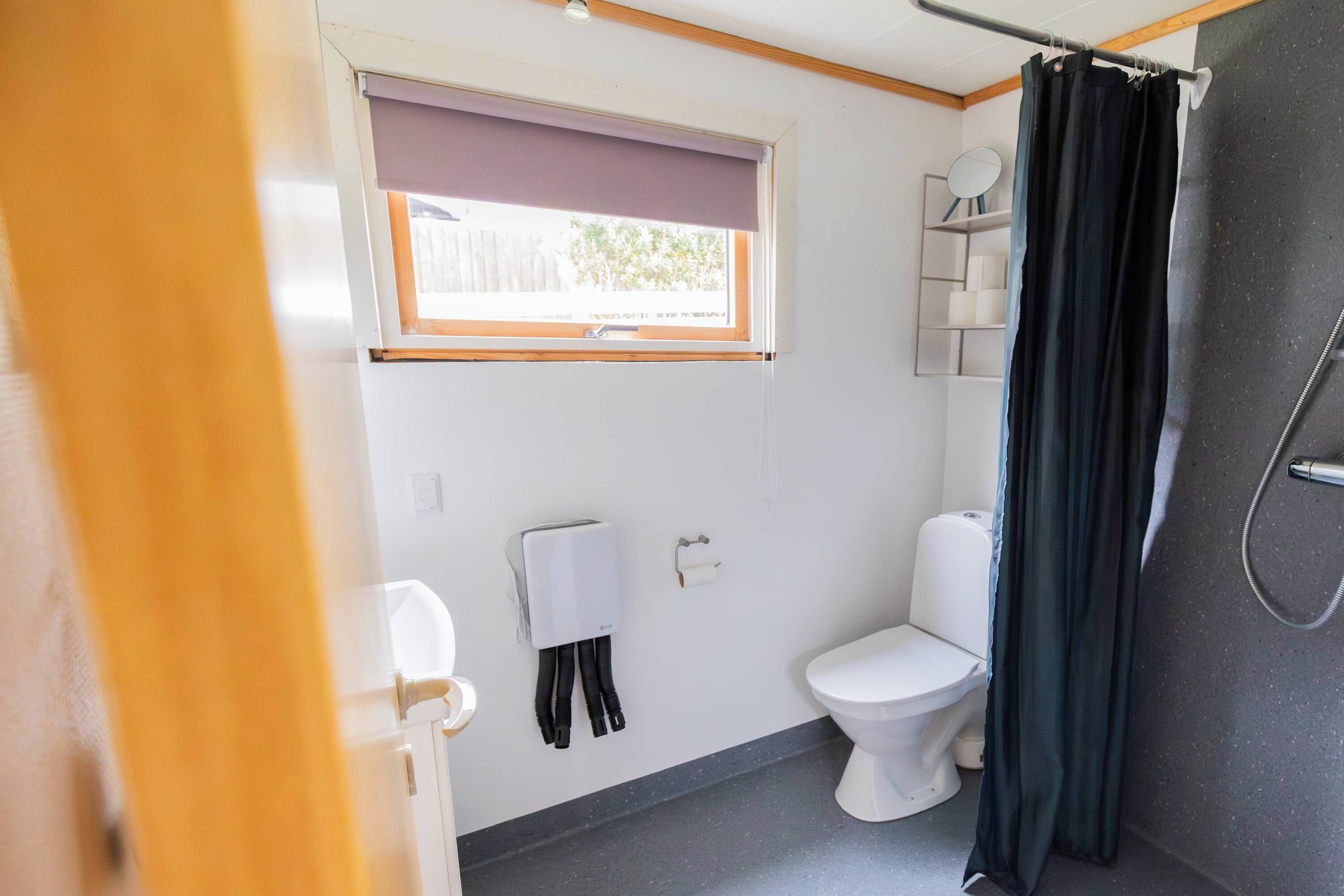 Ein kleines Badezimmer mit Toilette, Duschvorhang und Fenster mit Jalousie.